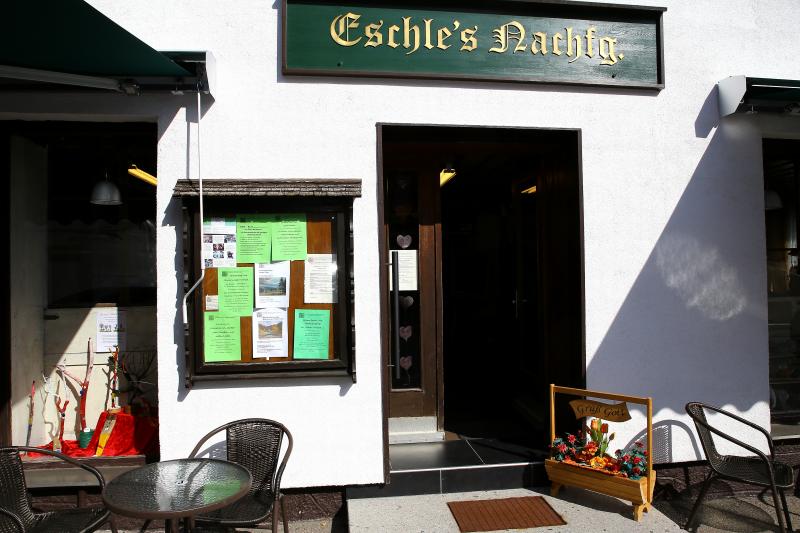 Eingang zum Vereinsheim Eschle mit dem Ladenschild „Eschles Nachfg.“, einem Schaukasten mit Aushängen und Tischen auf dem Gehweg